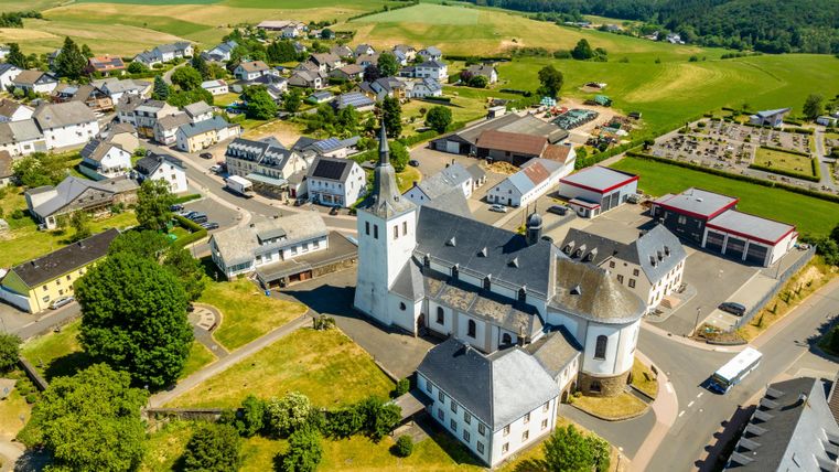 Ein malerisches Dorf mit einer Kirche im Zentrum und umgeben von grünen Hügeln. Die Architektur ist typisch für die ländliche Umgebung.