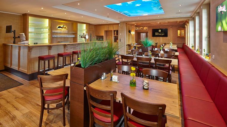 A cozy restaurant with wooden tables and red benches. The room is bright and has a ceiling with sky and clouds.