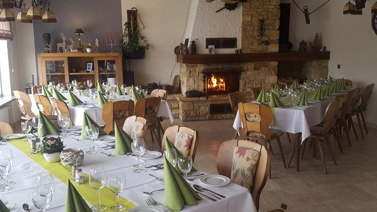 A cozy dining room with festively laid tables and green napkins. In the background, an open fire in the fireplace radiates pleasant warmth.