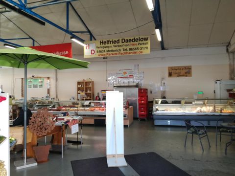 Ein Fleischereigeschäft mit Vitrinen voller Fleischwaren. Im Hintergrund sind Regale und eine große Infofläche sichtbar.