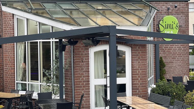 Een modern restaurant met een grote glazen façade. Buiten staan tafels en stoelen klaar.