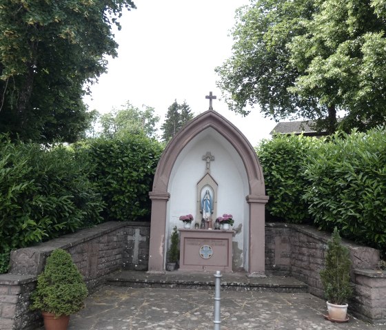Petite chapelle avec une statue de la Vierge Marie, entour&eacute;e d'arbres et de buissons. La chapelle a une croix sur le toit et des fleurs &agrave; l'int&eacute;rieur., &copy; TI Bitburger Land