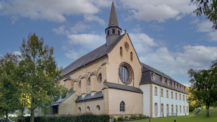 Eine beeindruckende Kirche mit einem spitzen Turm und großen Fenstern. Umgeben von Grünflächen und einem klaren Himmel.