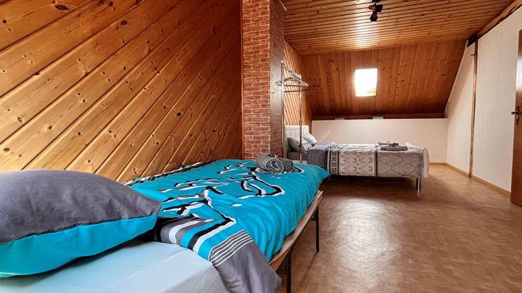 Een gezellige slaapkamer op de zolder met houten plafonds en twee bedden. De kamer is licht en uitnodigend met een raam dat licht binnenlaat.