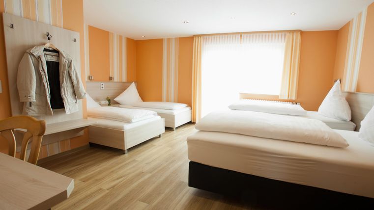 A bright room with orange walls. There are two beds, a small table, and a wardrobe visible.