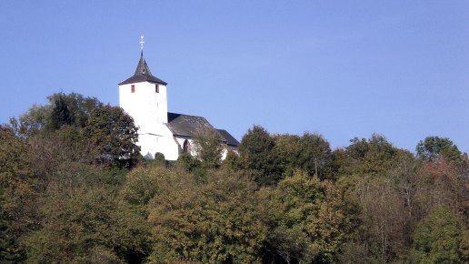 Die Kirche St. Apollonia in Gransdorf thront auf einem bewaldeten Hügel unter klarem, blauem Himmel., © Doris Pauels