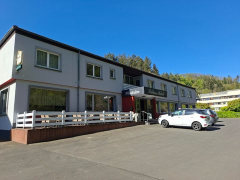 Ein kleines Gasthaus mit einer hellen Fassade und einem einladenden Eingangsbereich. Vor dem Gebäude stehen mehrere Autos parken.