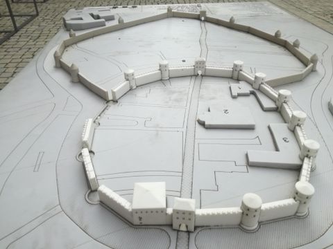 Ein Modell einer historischen Festung mit einer ovalen Mauer und mehreren Türmen. Die Struktur ist in hellen Farben gehalten und zeigt den Verlauf der ehemaligen Mauern.