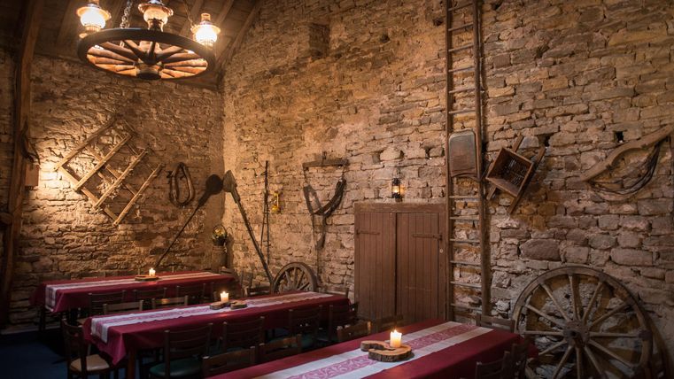 Ein rustikales Restaurant mit freiliegenden Steinmauern und Holzelementen. Die Tische sind mit roten Tischdecken dekoriert und von Kerzen beleuchtet.