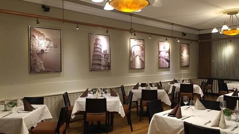 An elegant restaurant with white tablecloths and wooden floors. Framed pictures of iconic landmarks hang on the walls.