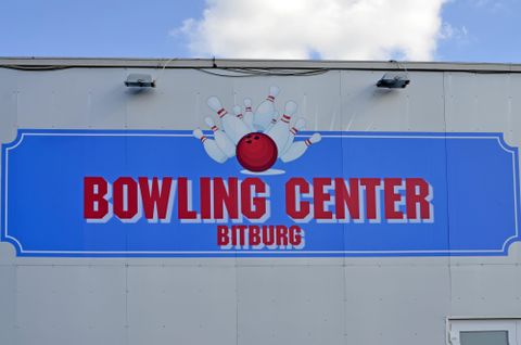 Un groupe d'amis joue au bowling dans une salle de bowling moderne. La femme au premier plan lance une boule de bowling rouge, tandis que ses amis regardent attentivement.