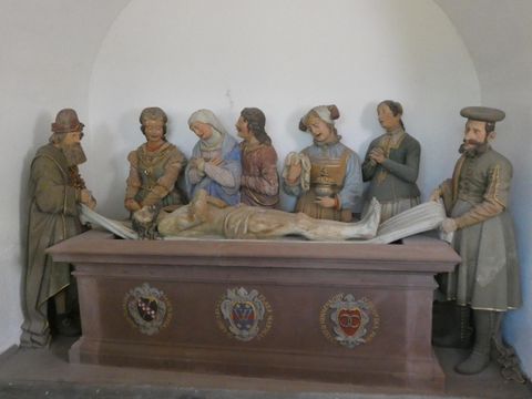 Eine Gruppe von Figuren, die eine biblische Szene darstellen. Sie stehen um eine Liege mit einer männlichen Figur, die tot zu sein scheint.