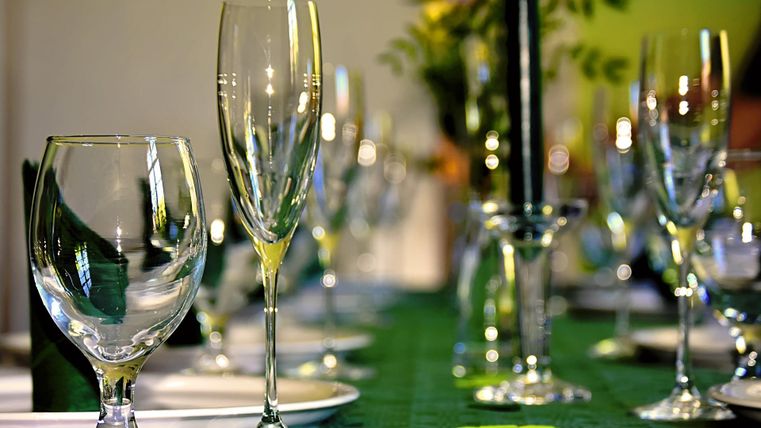A beautifully set table with glasses, candles, and a green table runner. In the background, floral decorations are visible.