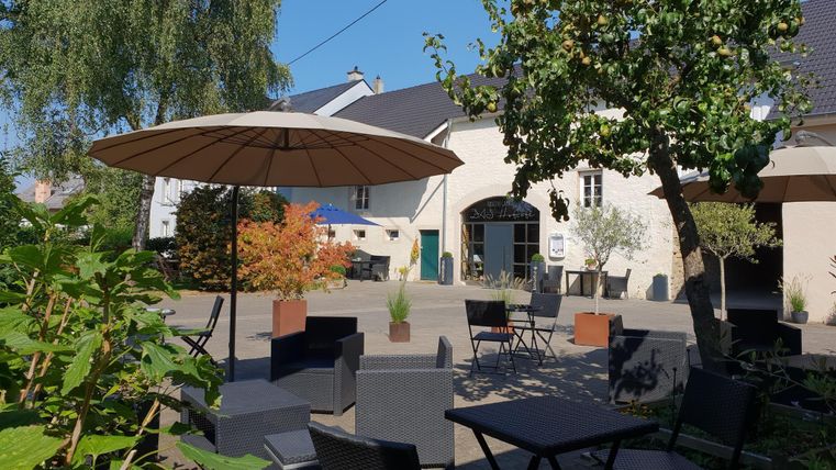 A cozy outdoor area with tables and chairs under a sunshade. Surrounded by trees and plants in an inviting atmosphere.