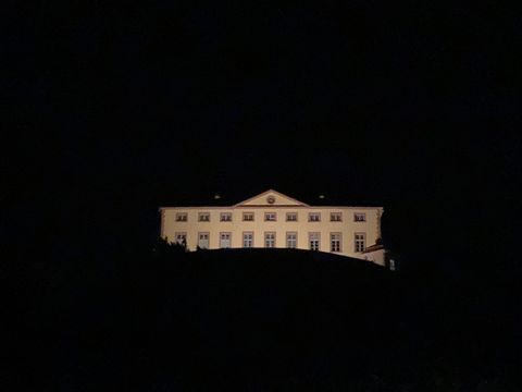Ein Gebäude, das nachts beleuchtet ist, steht auf einem Hügel. Der Himmel ist dunkel und die Umgebung ist kaum sichtbar.