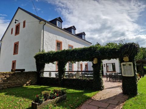 Ein schönes Gebäude mit einer weißen Fassade und roten Fensterrahmen. Draußen befindet sich ein bepflanzter Bereich mit Sitzgelegenheiten unter einem grünen Vordach.