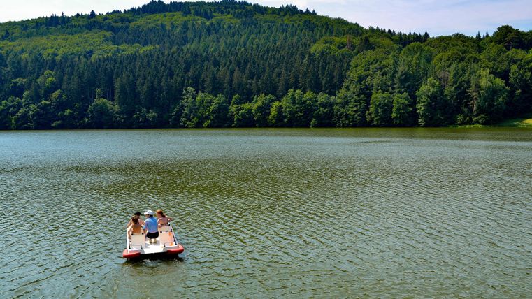 Een roeiboot met drie personen op een rustig meer. Op de achtergrond zijn beboste heuvels te zien.