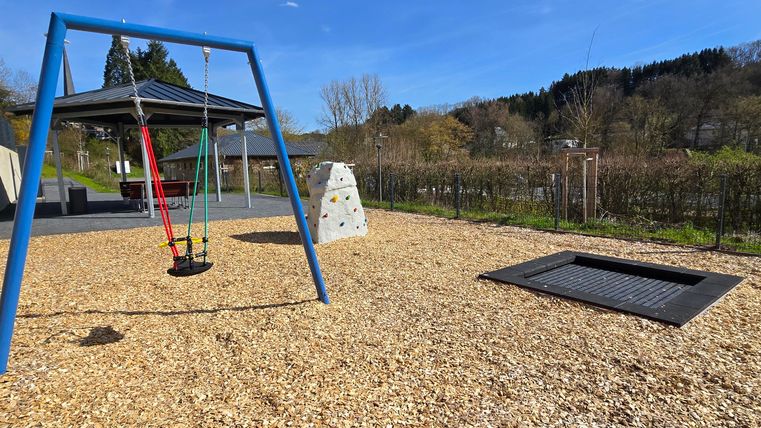 Een mooie speelplaats met een schommel, een klimwand en een trampoline. De lucht is helder en er is veel ruimte om te spelen.
