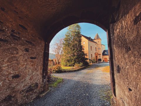 Einmaliger Blick durch einen Torbogen auf ein historisches Gebäude mit einem schönen Garten und Bäumen. Die Szenerie strahlt eine ruhige und idyllische Atmosphäre aus.