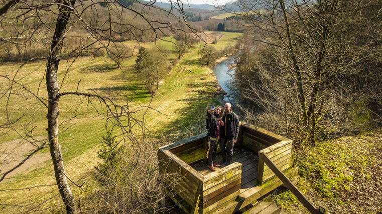 Two people take a selfie at a vantage point with a view of the Prümschleife and the surrounding landscape.
