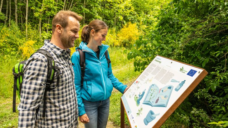Zwei Personen lesen eine Informationstafel im Grünen.