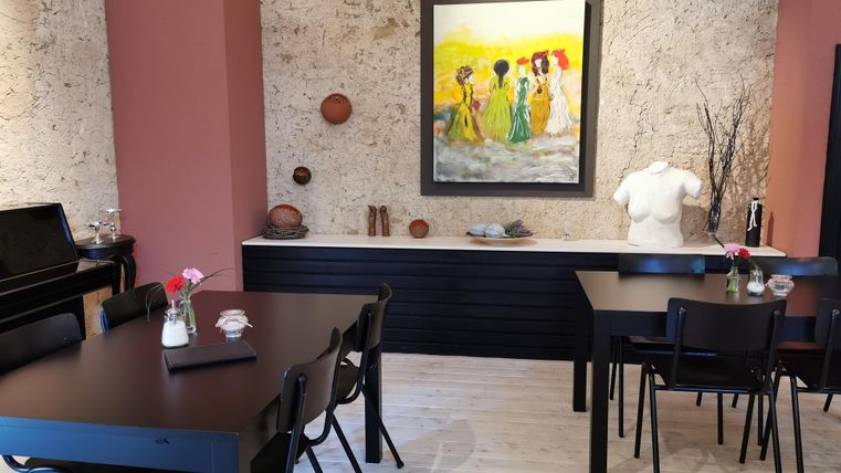 A stylish café with black tables and chairs.
On the wall hangs a colorful painting depicting a group of women.