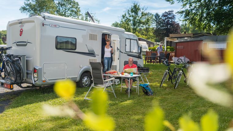Un camping-car est stationné sur un camping vert. Des gens sont assis à une table en plein air et profitent de leur temps.