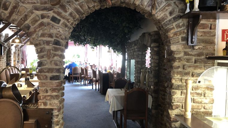 A cozy restaurant area with a stone arch and wooden furniture. The room is brightly lit and offers an inviting atmosphere.