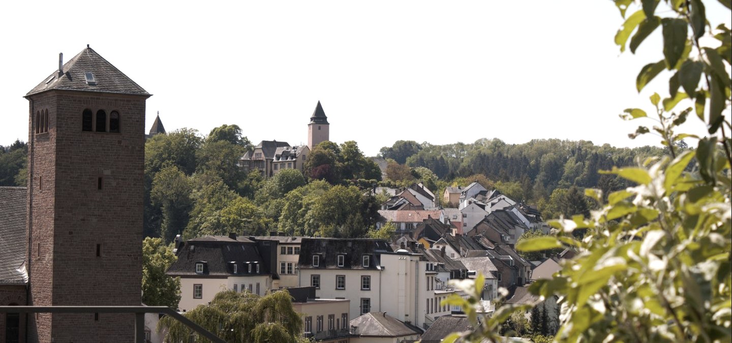 Panoramablick auf Kyllburg mit einem Kirchturm im Vordergrund, umgeben von H&auml;usern und gr&uuml;nen B&auml;umen unter blauem Himmel., &copy; TI Bitburger Land